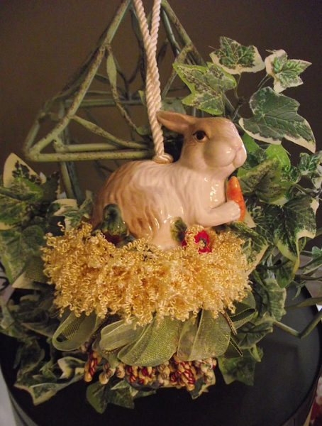 Beautiful handmade tassel with a bunny figurine in colors green and yellow, hanging from a fake plant stand. 