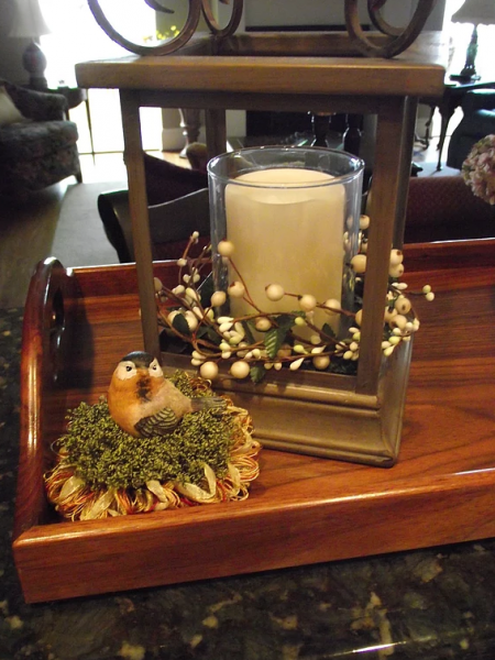 Cute bird figurine tassel in the color green with yellow and red accents sitting beside a candle holder. 